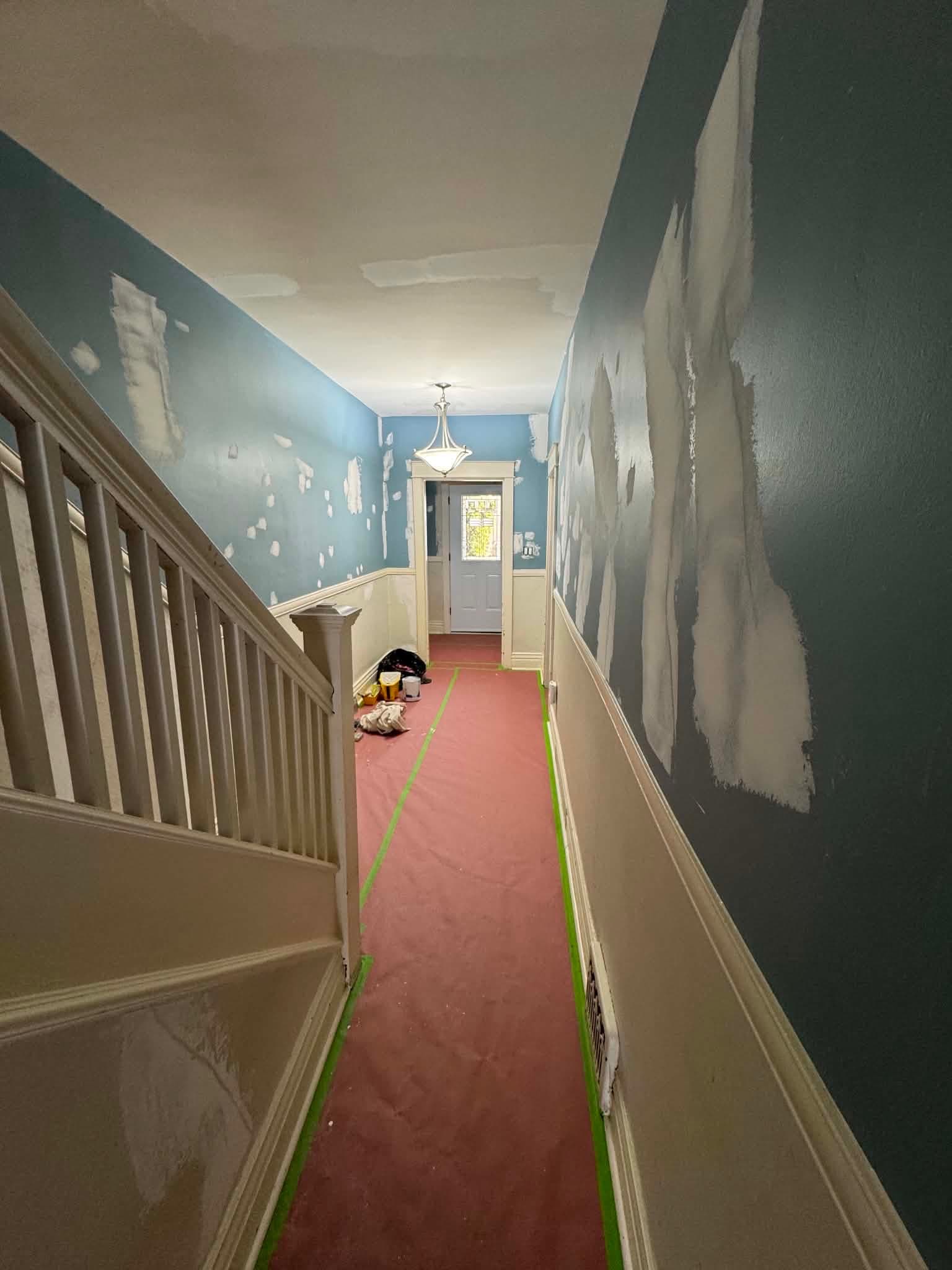 A hallway in an older Toronto home prepped for painting, with red floor-protection paper taped down the length of the floor and patched walls waiting for paint