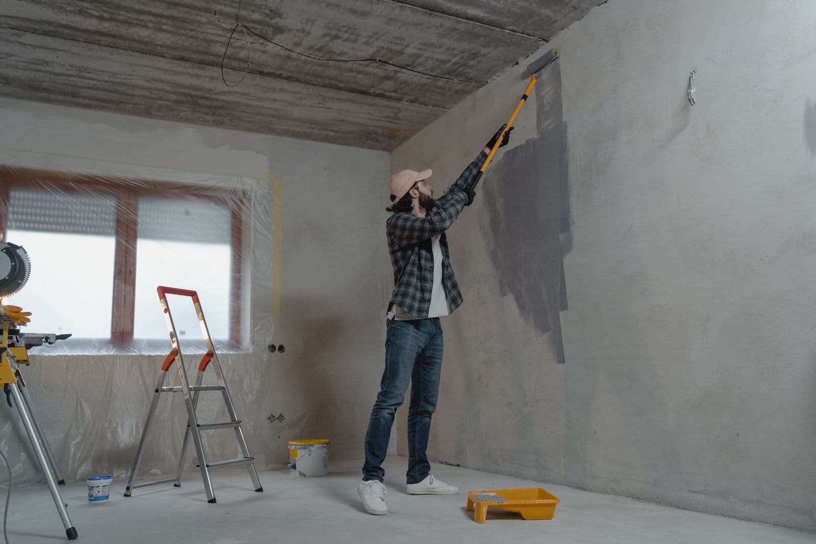 A painter using an extension roller to apply fresh grey paint to a condo wall mid-renovation